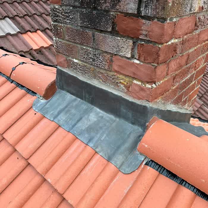 Lead apron and soakers finished tight against a chimney on a pantiled roof